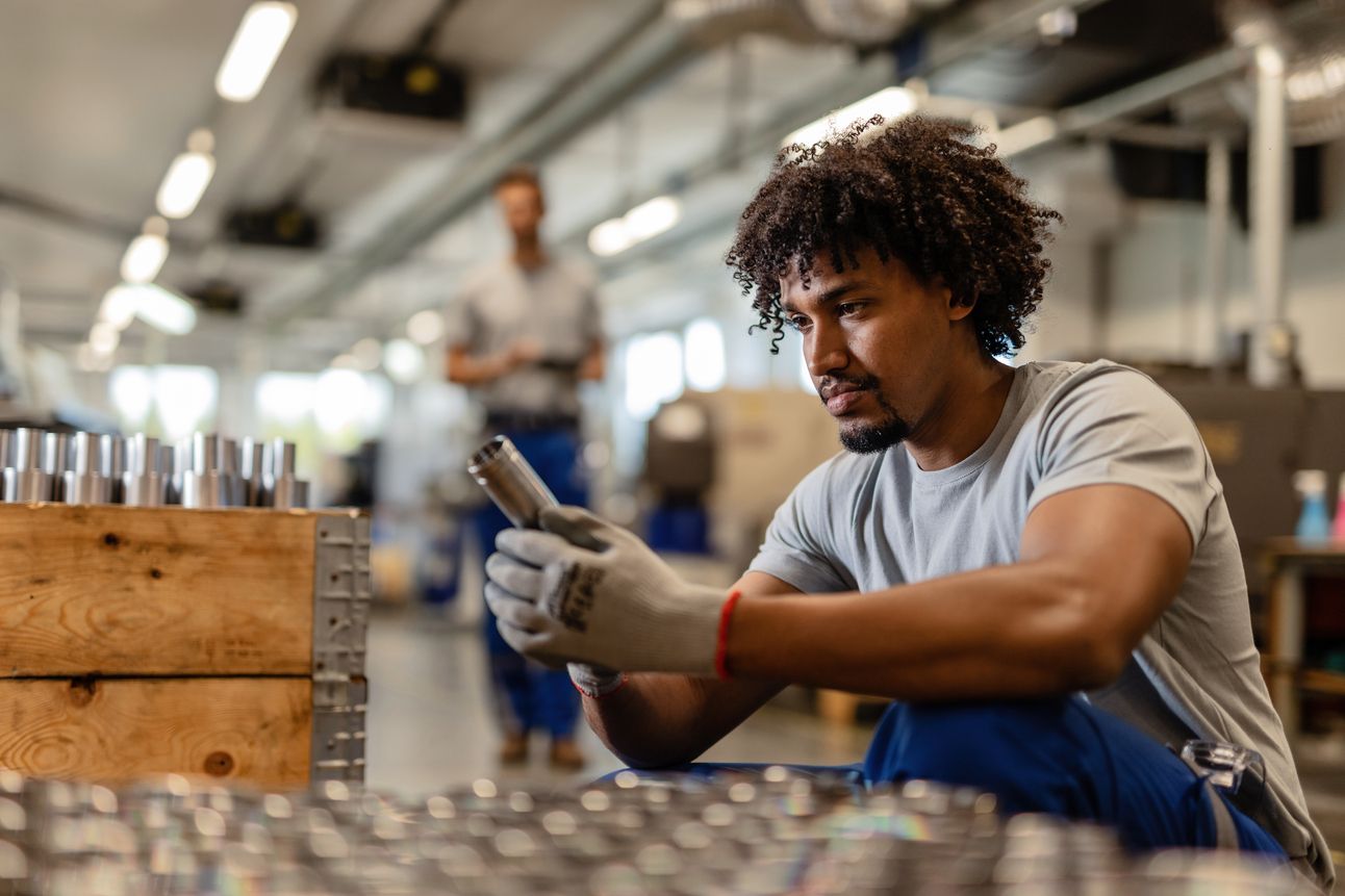 Young black worker examining stainless steel cylinder rod while working distribution warehouse